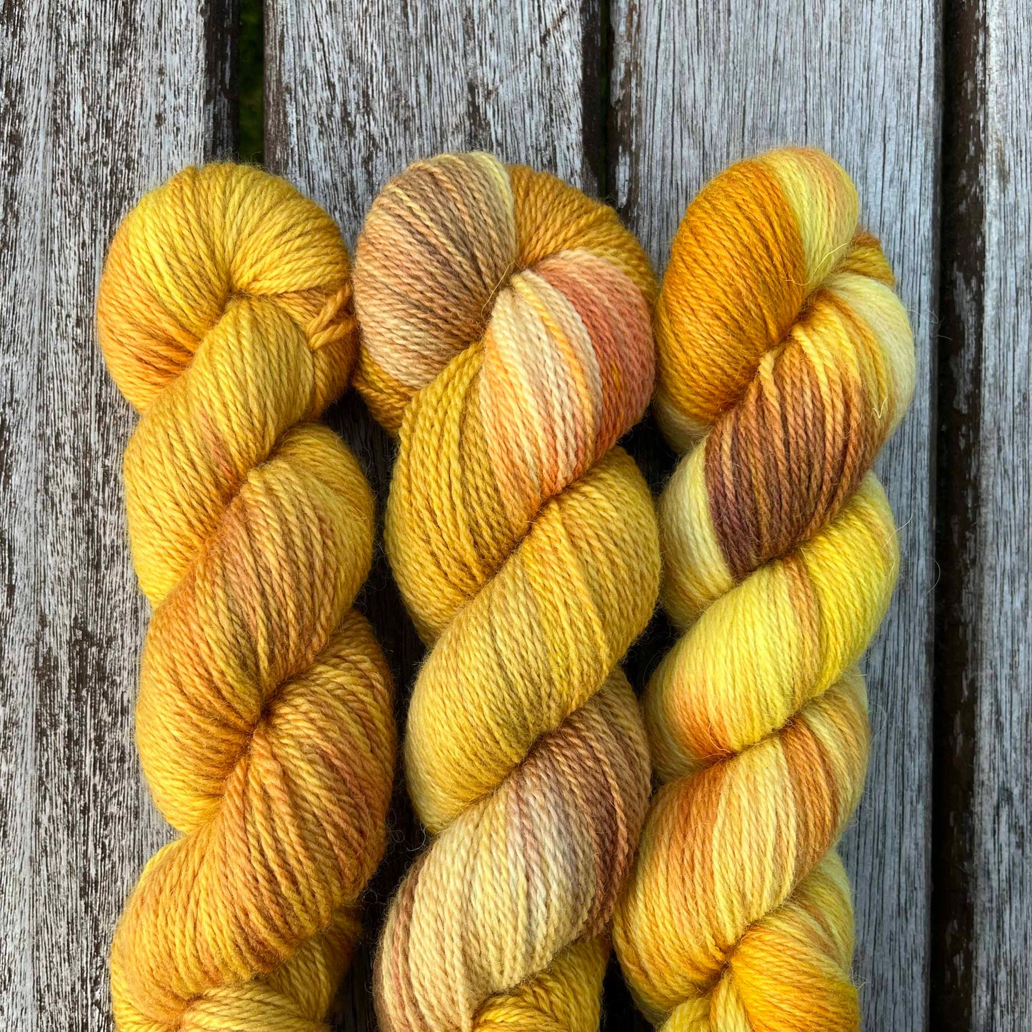 Three skeins of variegated golden yarn on a wood background.