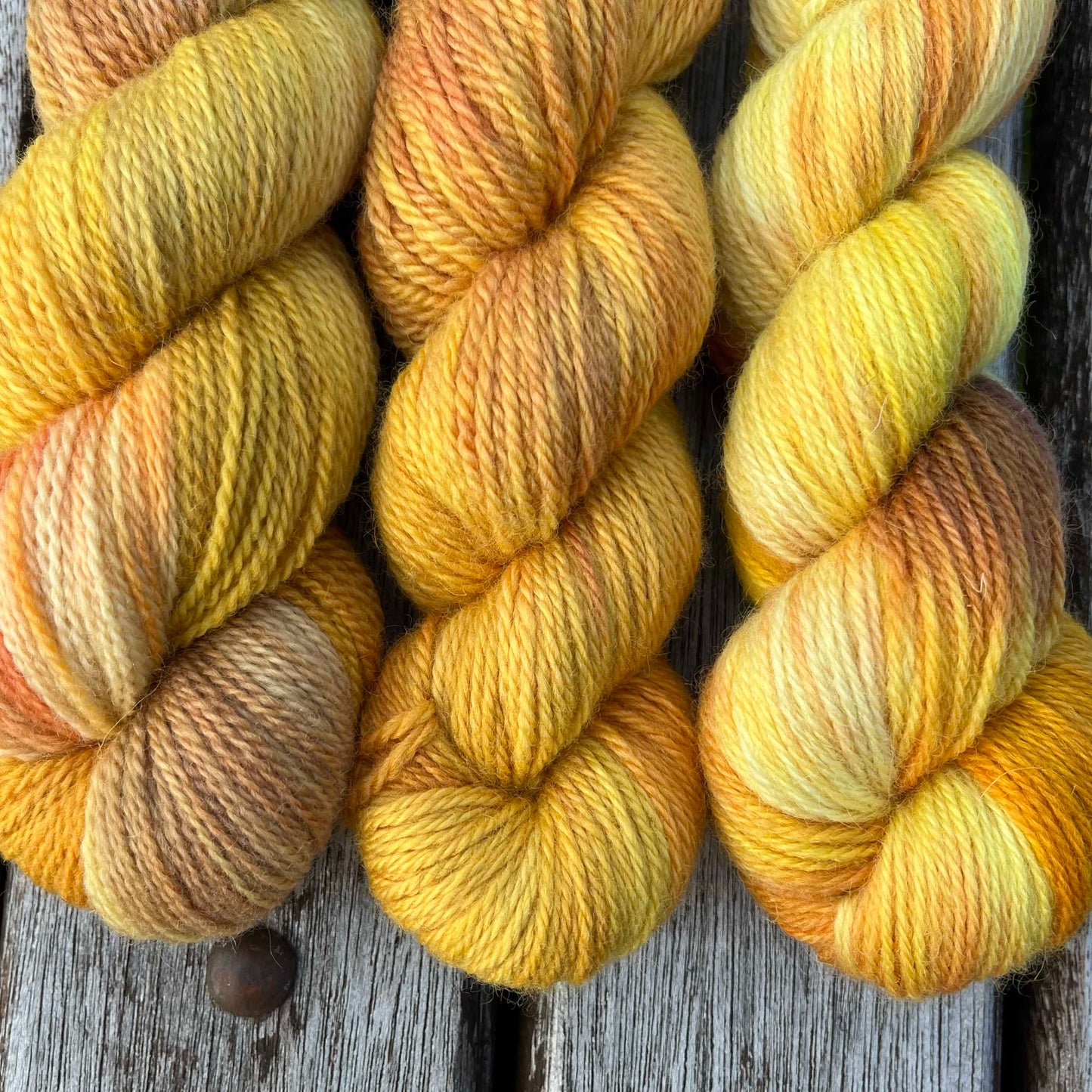 Three skeins of golden yarn descend into the photo over a wood background.
