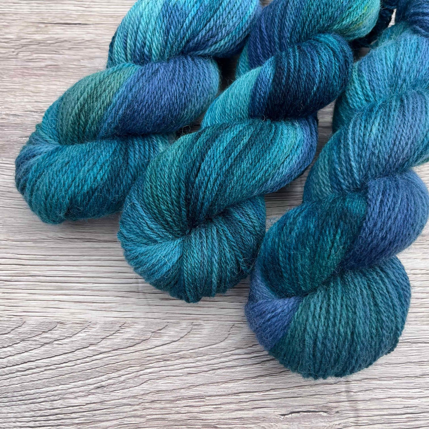 Three dark variegated skeins of teal, green and blue yarn.
