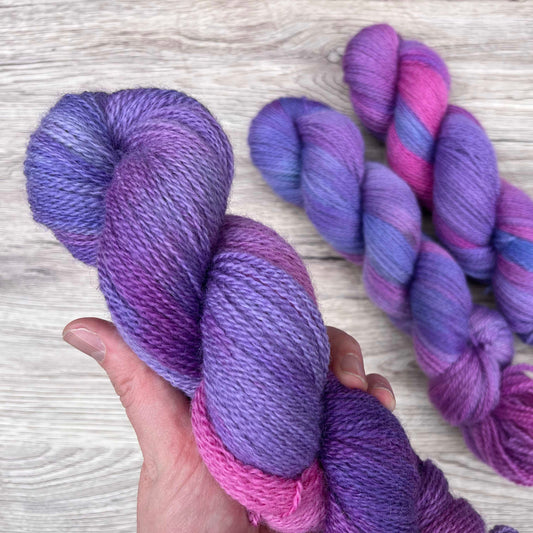 A white hand hold a skein of bright purple and pink yarn.