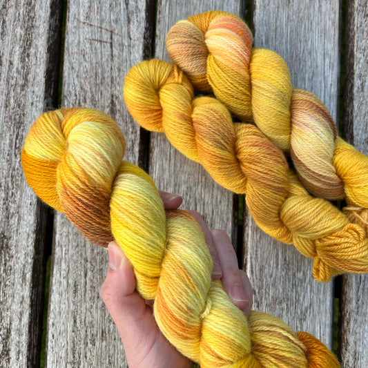 A white hand holds a skein of variegated golden yarn.