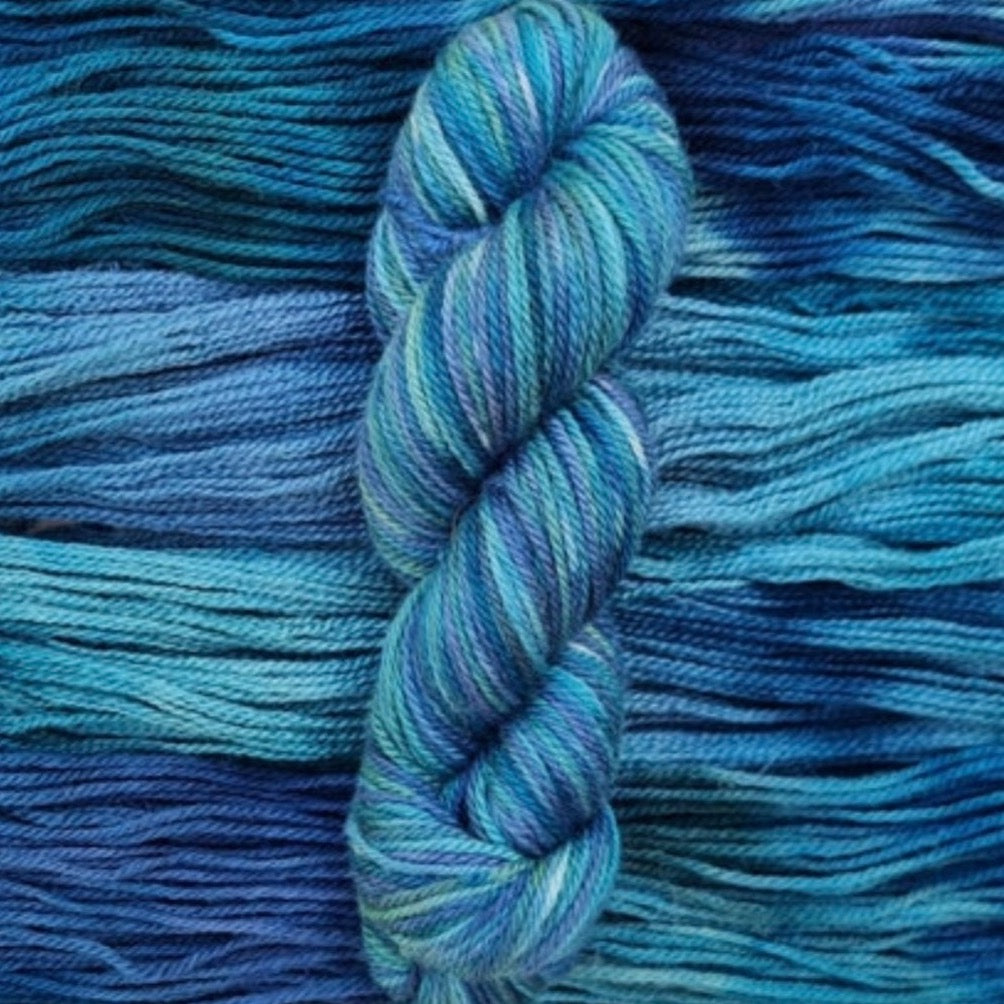 A dark skein of teal, blue and green yarn sits on a background of the same wool.