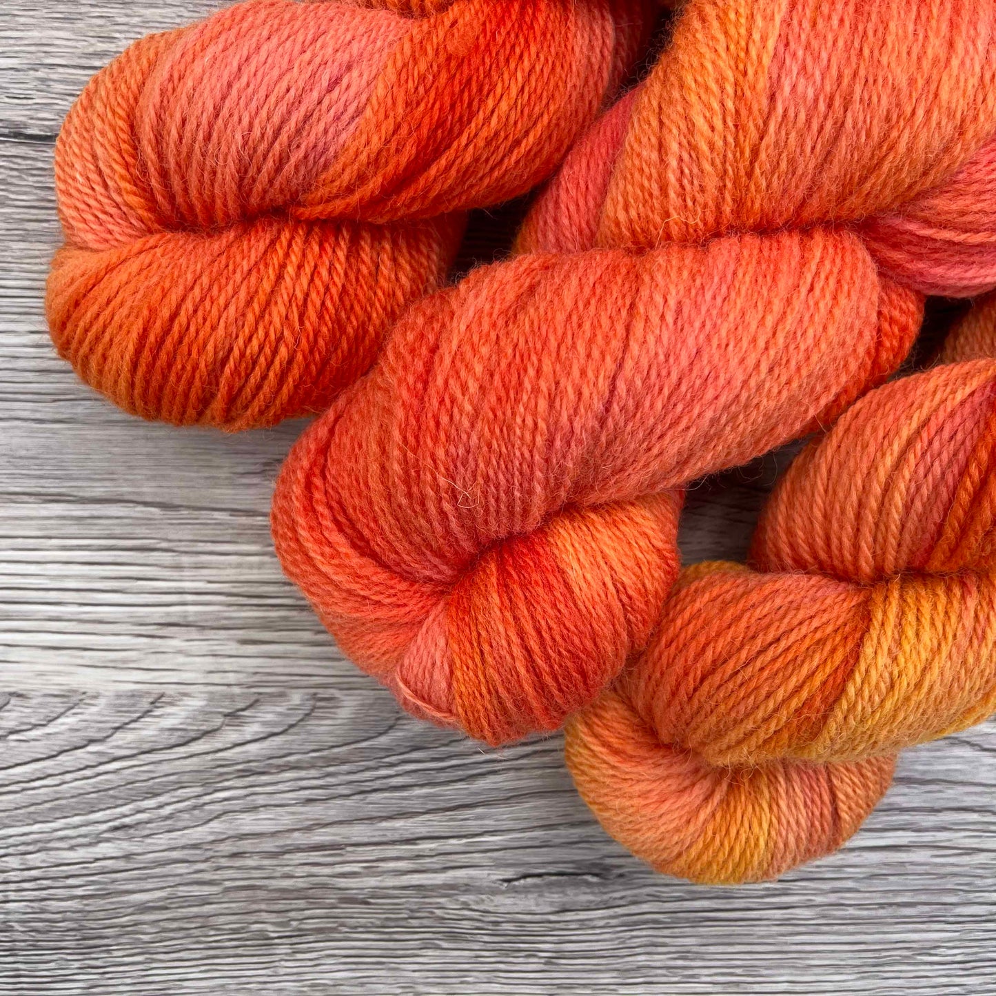 Three skeins of tonal peach yarn peek into the photo over a wood effect background.