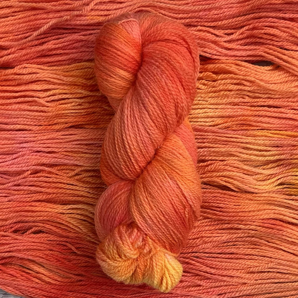 A skein of tonal peach yarn sits on a background of the same wool.