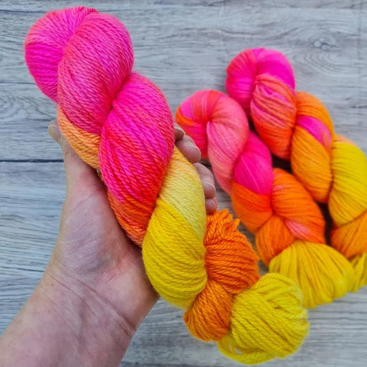 A white hand holds a skein of bright pink and yellow yarn.