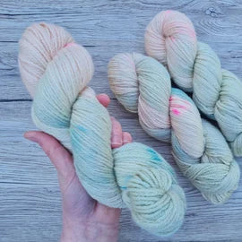 A white hand holds a skein of pastel pink and green yarn.