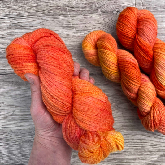 A white hand holds a plump skein of tonal coral yarn.