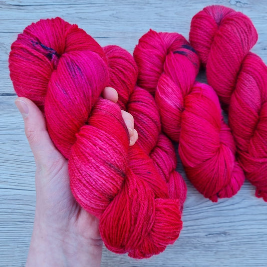 A white hand holds a vibrant red skein.
