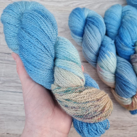 A white hand holds a skein of blue yarn.