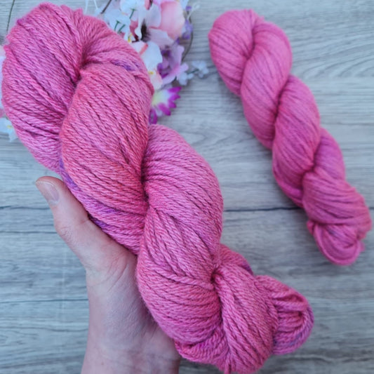 A white hand holds a skein of tonal pink.