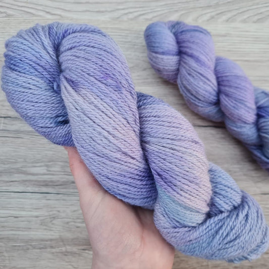 A white hand holds a skein of purple yarn.