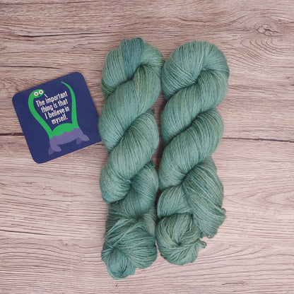 Two skeins of tonal teal yarn on a wood-effect background.