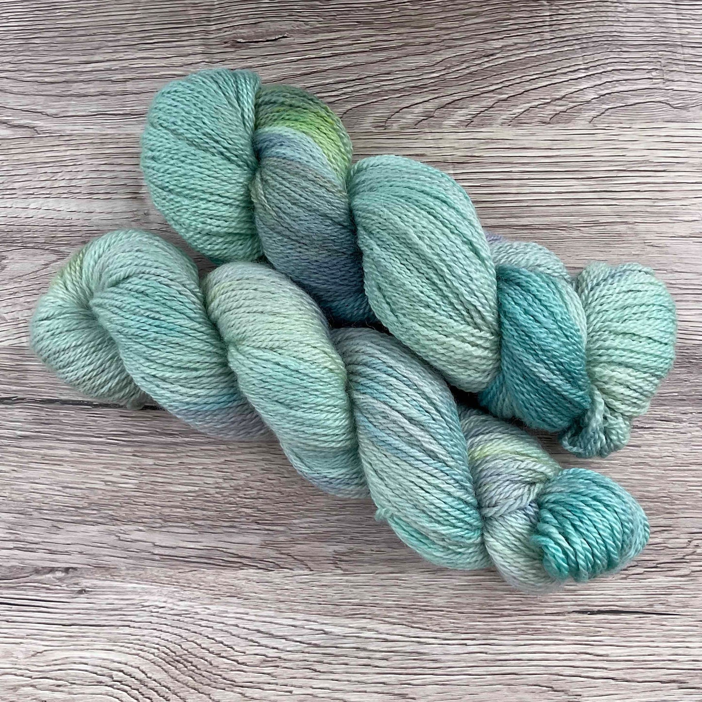 Two skeins of blue yarn on a wood effect background.