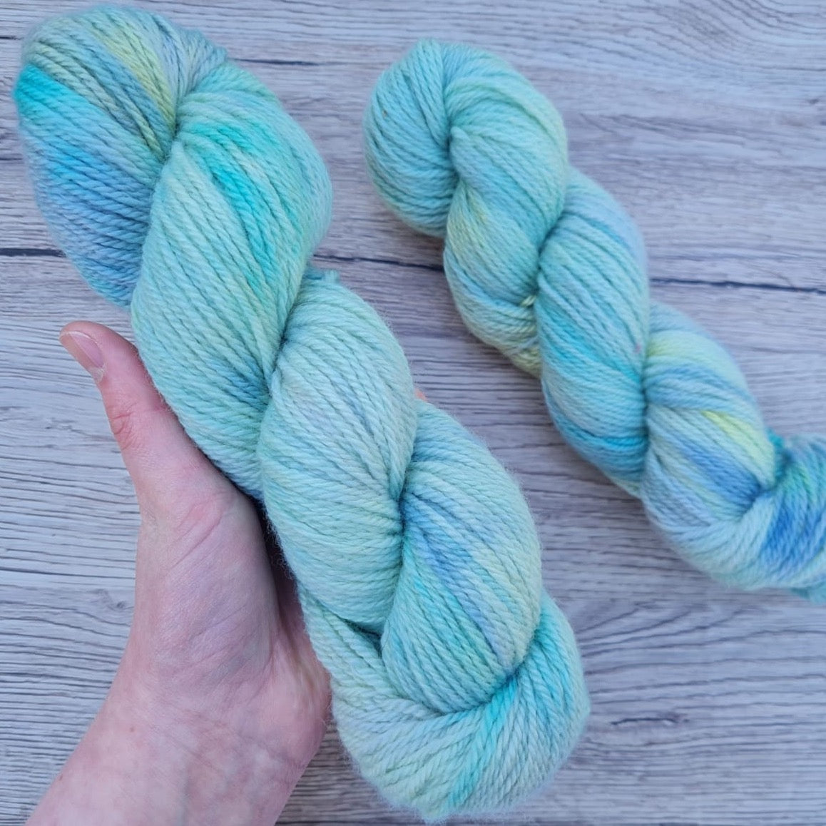 A white hand holds a skein of variegated cool blue yarn.