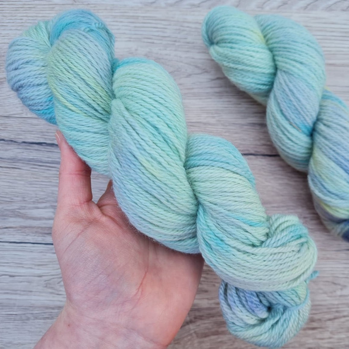 A white hand holds a skein of cool blue yarn.