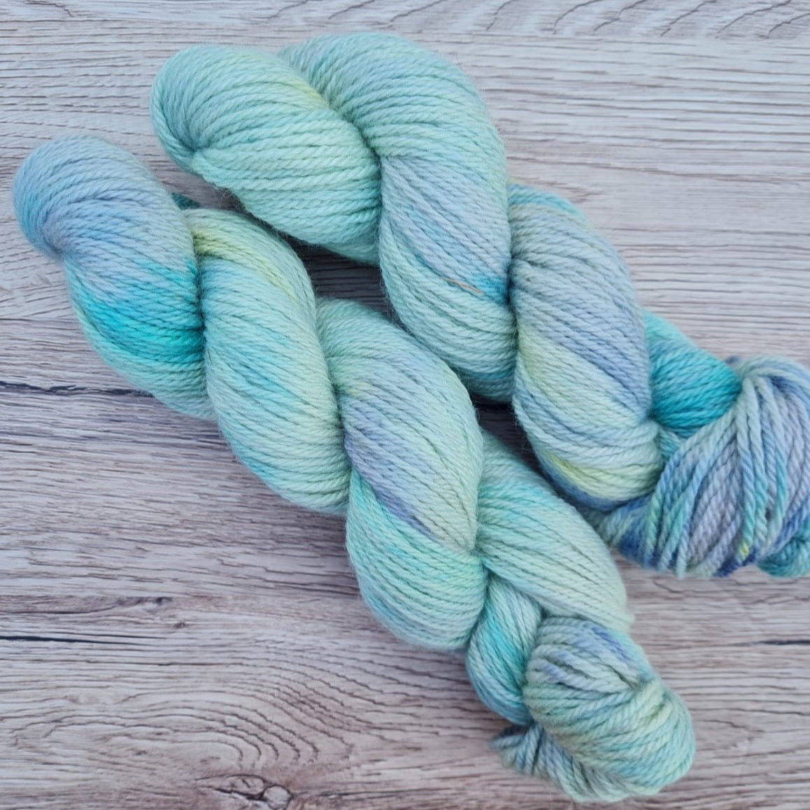 Two skeins of cool blue yarn on a wood background.